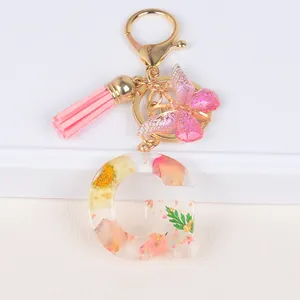 Detailed macro view of resin letter G keychain with dried flowers and pink tassel