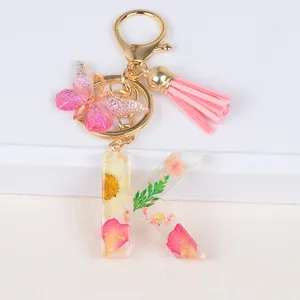 Detail of resin letter K keychain with real dried flowers, gold foil and pink tassel