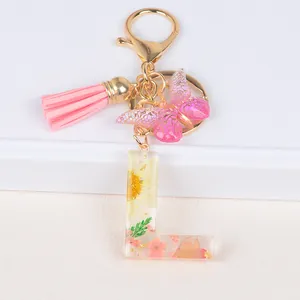 Floral resin letter L keychain with pink butterfly and tassel on white steps