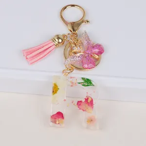 Detail of resin letter R keychain with pink dried flowers, gold foil, and butterfly tassel