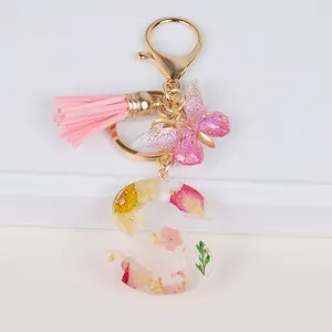 Detail of resin letter S keychain with real dried flowers, gold leaf, and pink tassel