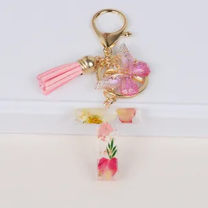 Detail of resin letter T keychain with dried flowers, butterfly charm and pink tassel