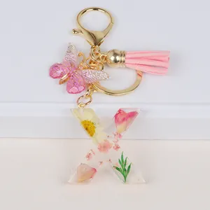 Close-up of resin letter X keychain with yellow dried flowers, pink butterfly and tassel
