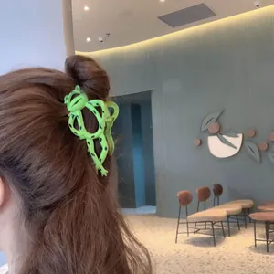 Detail of cute green frog hair claw clip worn on long brown hair for styling