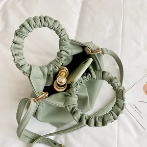 Sage green ruched cloud bag with top handles, crossbody strap, and storage items