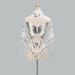 Detailed close-up of white lace shawl featuring black butterfly embroidery and long tassels