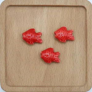 Tre perle di pesce in ceramica rossa lucida per gioielli fai-da-te su vassoio in legno