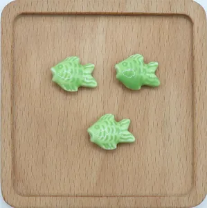Tre perle di pesce in ceramica verde con scaglie su vassoio in legno per gioielli fai-da-te