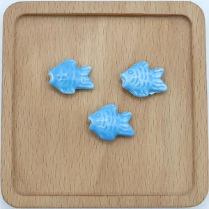 Dettaglio di tre perle di pesce in ceramica smaltata blu per gioielli fai-da-te su legno