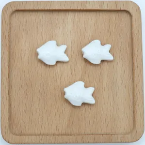 Dettaglio di tre perle a forma di pesce in ceramica bianca per gioielli fai-da-te