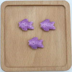 Dettaglio di tre perline in ceramica a forma di pesce viola su un vassoio di legno