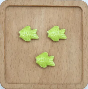 Tre perline a forma di pesce in ceramica verde chiaro su vassoio in legno per gioielli