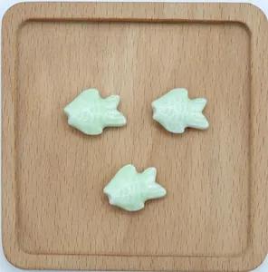 Dettaglio di perline in ceramica a forma di pesce verde chiaro per gioielli fai da te in legno