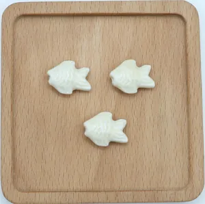 Vista dettagliata di tre perline a forma di pesce in ceramica crema per gioielli fai-da-te