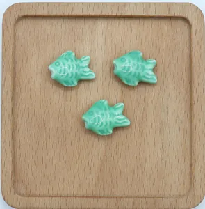 Dettaglio di tre perline in ceramica turchese a forma di pesce su vassoio di legno rustico