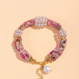 Detailed view of woven pink tourmaline and pearl bracelet with golden lobster clasp and chain