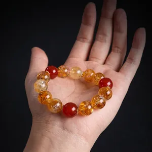 Detailed view of amber and dark red beaded bracelet held in hand on dark background