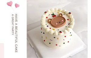 Top view of cream cake with brown bear topper, cherries, and colorful sprinkles