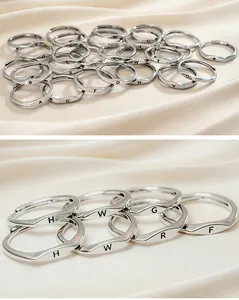 Close-up of polished silver alphabet open rings with wave design on silk background