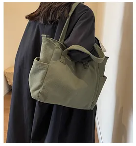 Corduroy tote bag in olive green showing side view on shoulder with soft lighting
