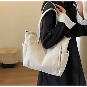 Detail of off-white corduroy tote bag showing the side pocket and front zipper texture