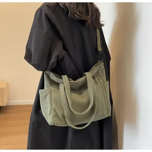 Rear view of model wearing green corduroy tote bag with adjustable shoulder strap and side pockets