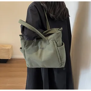 Detail of green corduroy tote bag showing side pockets and metal D-ring attachment