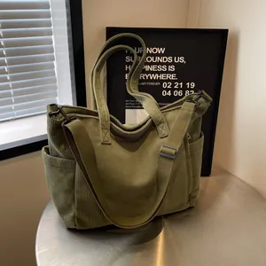 Green corduroy tote bag with dual handles and adjustable strap on a metal table