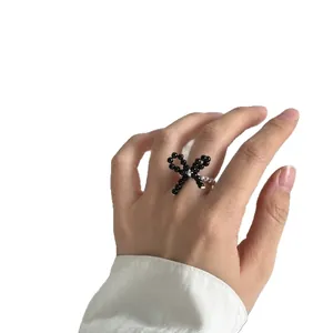 Hand wearing a sweet black beaded bow ring with silver beaded band on white background