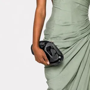 Detail of a black glossy irregular clutch bag with metallic clasp on a sage green dress