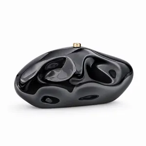 Macro detail of high-gloss black acrylic evening clutch with gold metal cylinder clasp