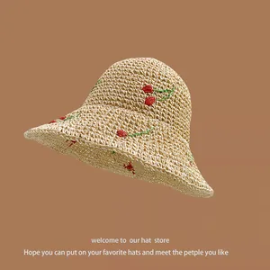 Close-up of beige straw sun hat featuring detailed red cherry embroidery and woven texture
