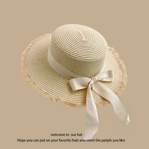 Detail of beige woven straw hat featuring a stylish ribbon bow and natural frayed edges