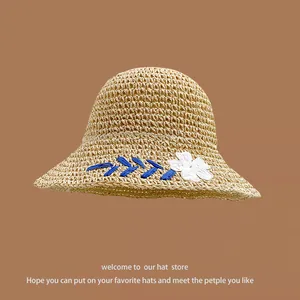 Detailed close-up of straw sun hat featuring a 3D white fabric flower and blue embroidery