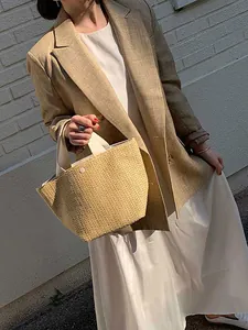 Close-up of a woven straw bucket bag with cream handles held against a white wall