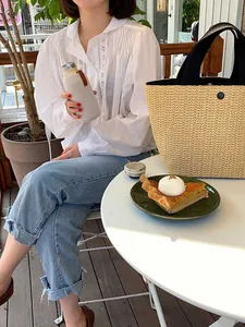 Detail of a woven straw bucket bag with black handles and round button closure on a table