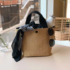 Detail of hand-woven straw bucket bag with black handles, polka dot scarf and sunglasses