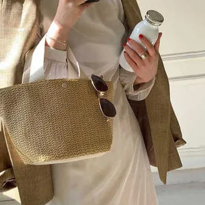 Detail of straw woven bucket bag featuring cream fabric handles and a metal snap closure