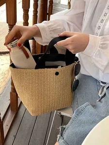 Woven straw bucket bag with black handles and snap closure on a sunny outdoor terrace