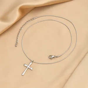 Vue détaillée du collier pendentif croix argenté sur fond de soie couleur champagne