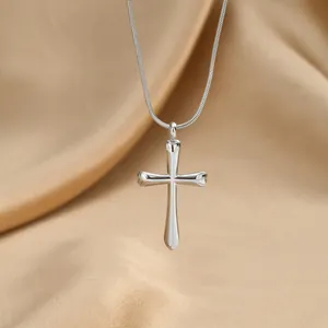Détail du collier avec pendentif croix en argent poli sur un fond de satin champagne