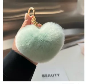 Détail d'un porte-clés cœur en fausse fourrure vert menthe avec fermoir doré tenu à la main