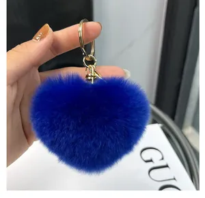Détail d'un porte-clés en peluche en forme de cœur bleu roi avec fermoir doré en main