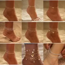 Close-up of assorted gold and silver anklets with charms on beach sand background