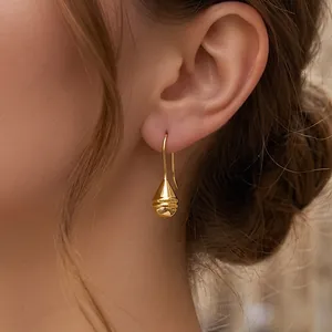 Detailed close-up of golden textured teardrop earring with horizontal stripe pattern