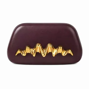 Gros plan d'une pochette en cuir bordeaux avec décoration métallique dorée sculpturale