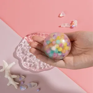 Close-up of a hand squeezing a colorful maltose bead stress ball toy in a dreamy setting
