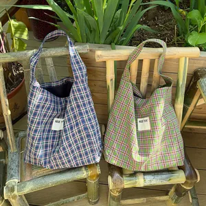 Close-up of two checkered fabric tote bags with SEE YOU labels on a bamboo chair