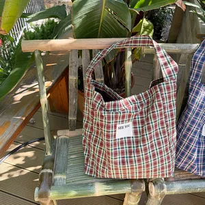 Close-up of vintage plaid canvas tote bags with 'SEE YOU' label on a bamboo chair
