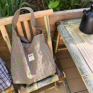 Detail of green and purple plaid tote bag with See You label on bamboo chair